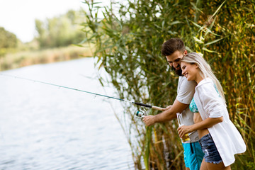 Naklejka na ściany i meble Young couple enjoying fishing on sunny day at a calm lake
