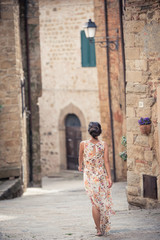 Fototapeta na wymiar Young asian girl walking in Monticchiello town on summer day. Amazing promenade with traditional old stone houses - Tuscany, Italy, Europe