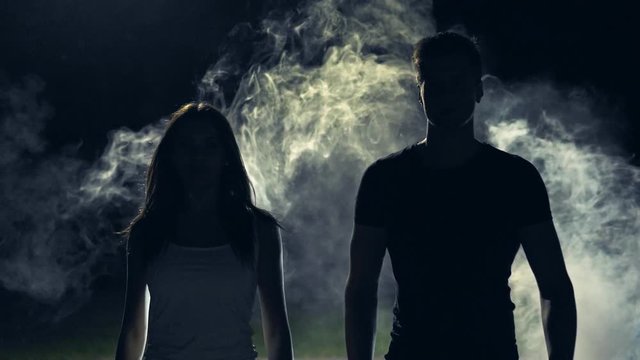 The man and woman walking in a dark through the smoke cloud. slow motion