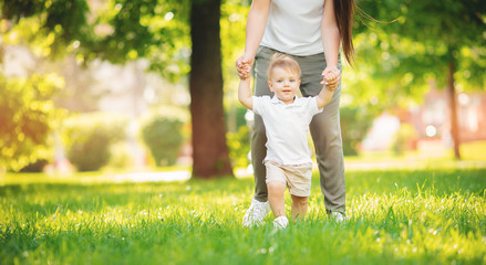 Happy smiling child boy makes first step in park, mom helps