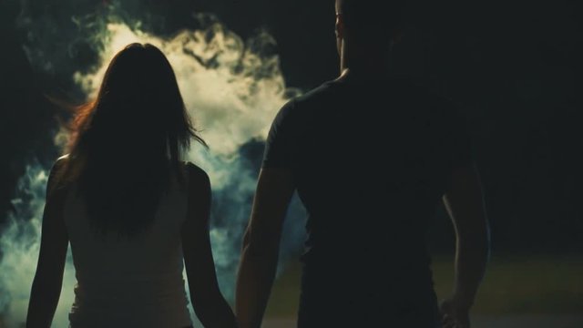 The couple walking in the dark street through a white smoke. slow motion