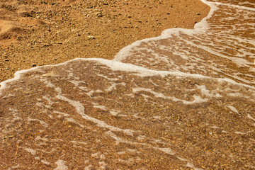 Summer background of hot sand with sea or ocean wave bubbles with copy space for card or advertisement at dawn or sunset