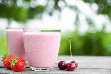 A glass of fresh cold smoothie with berries and cherrys on a wooden table, summer set, outdoor greed blured background,boke.