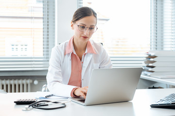 Doctor doing paperwork on computer sitting on desk