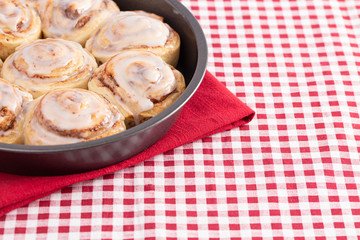 Pan of Frosted Cinnamon Rolls on a Red and White Plaid Tablecloth