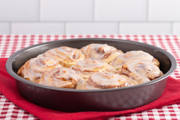 Pan of Frosted Cinnamon Rolls on a Red and White Plaid Tablecloth