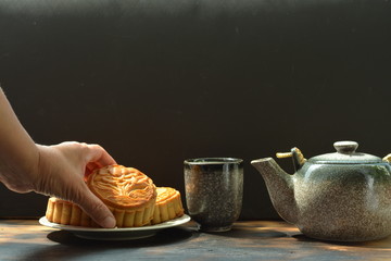 moon cake with hand and tea in a cup and tea pot on a black wooden black background