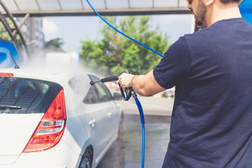 Man washing his car with pressurized water in car wash outdoors.