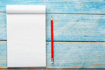 Notepad with red pencil on a blue wooden table background, for education, write goals and deeds