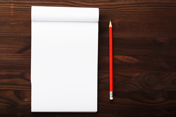 Notepad with red pencil on a brown wooden table background, for education, write goals and deeds