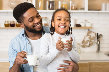 Black girl and her father are laughing while drinking milk