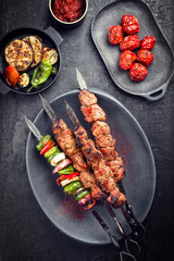 Traditional Russian shashlik on a barbecue skewer with vegetable and sumach paste as top view on a modern design plate