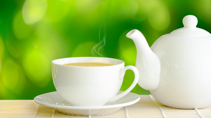 White cup of green tea and teapot on wooden table.