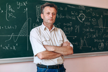 Teacher  standing folded hands next  the blackboard looking at the camera.- Image © speed300