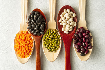 Fototapeta na wymiar Different kinds of beans in spoons on white background