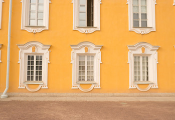 Fototapeta na wymiar Window of an old building, palace. The frame is made of stucco in the Baroque style. White linen on a yellow background of the walls (ocher). Grand Peterhof Palace. Summer is a sunny day.