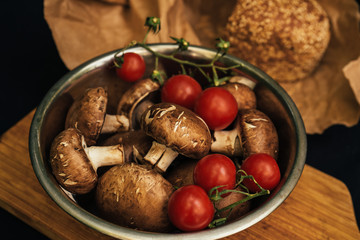 Champignons mushrooms and cherry tomatoes in plate on black background