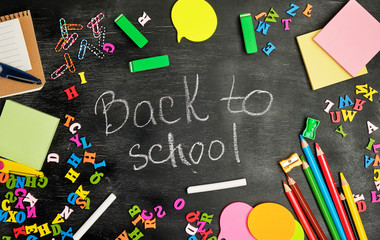 school supplies: multicolored wooden pencils, notebook, paper stickers, paper clips, pencil sharpener and white chalk inscription