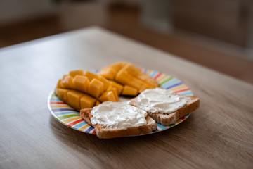 Cheese spread toasts with mango cut in cubes on a colorful plate on a wooden table