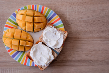 Cheese spread toasts with mango cut in cubes on a colorful plate on a wooden table