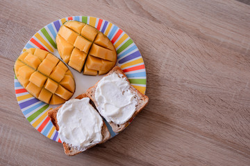 Cheese spread toasts with mango cut in cubes on a colorful plate on a wooden table