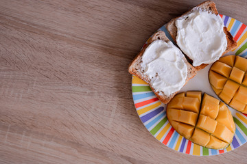 Cheese spread toasts with mango cut in cubes on a colorful plate on a wooden table