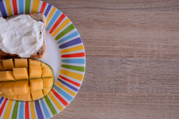 Cheese spread toasts with mango cut in cubes on a colorful plate on a wooden table