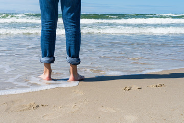 A teen boy stands on the sand facing the sea and sees off the summer. Concept. Summer is over. Seaside.