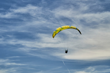 A tandem paraglider and with a yellow and blue parachute and high altitude clouds.