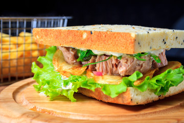 American fast food. Juicy tuna sandwich with chips, lettuce and french fries on a dark background. Club food.