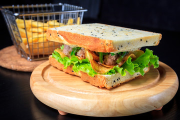 American fast food. Juicy tuna sandwich with chips, lettuce and french fries on a dark background. Club food.