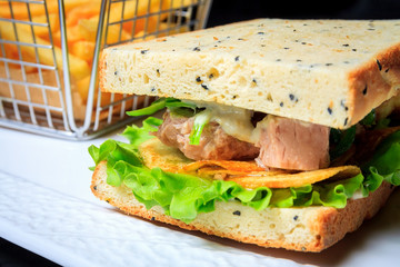 American fast food. Juicy tuna sandwich with chips, lettuce and french fries on a dark background. Club food.
