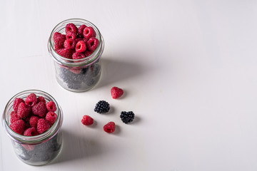 Raspberry and blackberry sweet organic juicy berries in two glass jars on white wooden table background