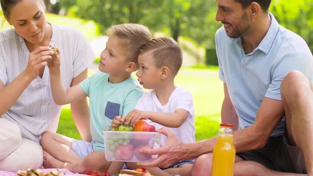 family, leisure and people concept - happy mother, father and two little sons eating fruits on picnic at summer park