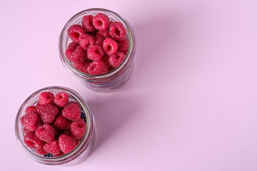Raspberry and blackberry sweet organic juicy berries in two glass jars on pink paper background, copy space
