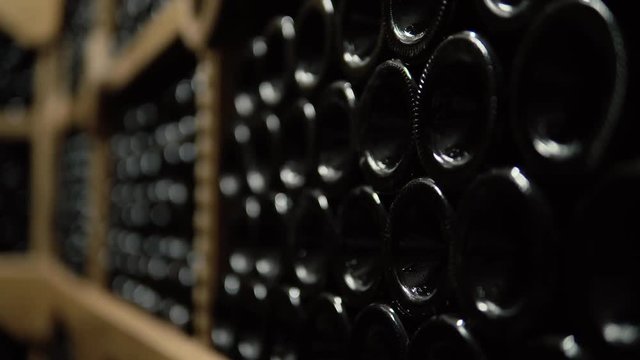 Wine bottles lying in stack at cellar. Glass bottles of red wine stored in wooden shelving in stone cellar. Interior underground wine cellar in winery