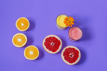 Still life. Two glass glasses filled with freshly squeezed orange and grapefruit juice, decorated with a flower stand on a bright purple background. Sliced ​​red grapefruit, orange oranges. Close-up. 