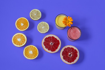 Still life. Two glass glasses filled with freshly squeezed orange and grapefruit juice decorated with a flower stand on a bright blue background. Cut slices of red grapefruit, orange oranges, yellow l