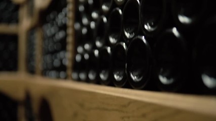Wine bottles lying in stack at cellar. Glass bottles of red wine stored in wooden shelving in stone cellar. Interior underground wine cellar in winery