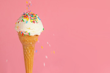 summer creative concept with ice cream cone and dynamic strewed sprinkles on pink background