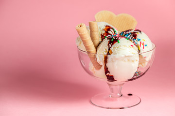 scoops of sundae ice cream in glass bowl with chocolate sauce, strewed sprinkles and cookies on pink background - Powered by Adobe