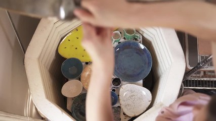 Oven for baking ceramics. Close-up of woman's hands opening the oven and taking out baked pottery plates. Ceramic dishes creation