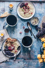 Healthy oatmeal breakfast with red currants, raspberry, grape and boiled egg with toast and coffee on a rustic blue background