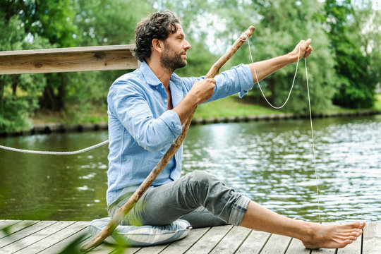 Man sitting on platform at the waterside with selfmade fishing rod
