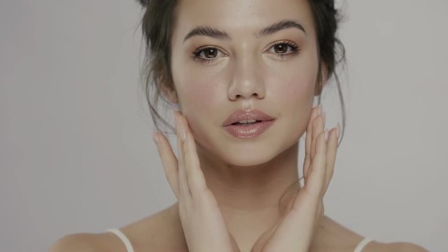 pretty woman with big dark eyes and perfect skin moisturizing her face with both arms