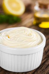 Mayonnaise sauce in white bowl with parsley, lemon and oil in the back (Selective Focus, Focus in the middle of the mayonnaise)