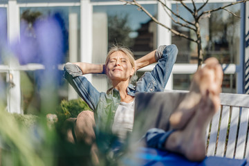 Smiling woman with laptop relaxing on garden bench