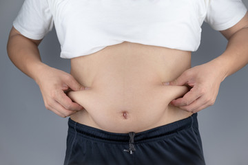 Naklejka premium Asian man are showing belly and raising hands catching the Fat at paunch.