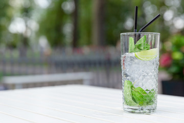 Mojito cocktail with lime and mint in glass on a white wooden table in outdoor restaurant