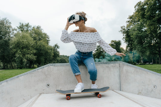 Young woman with skateboard wearing VR glasses in a skatepark